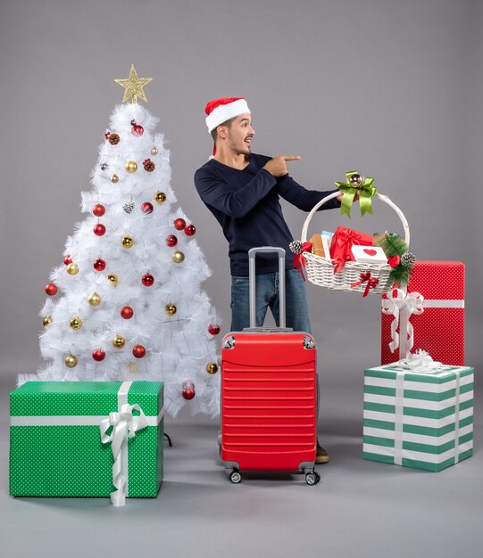 Front view young man with santa hat showing gift basket on grey isolated