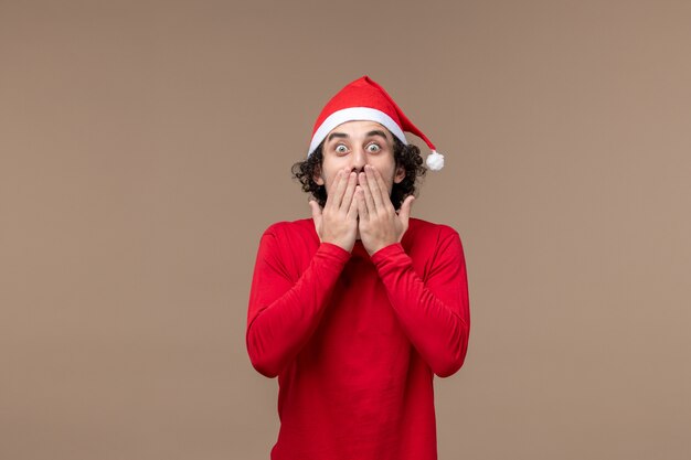 Вид спереди молодой человек с шокированным выражением лица на коричневом фоне рождественских эмоций