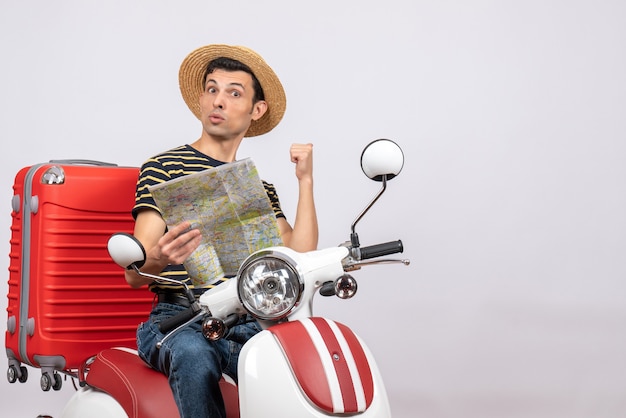 Front view of young man with straw hat on moped holding map pointing behind