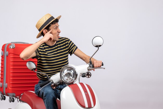 Front view of young man with straw hat on moped looking at right