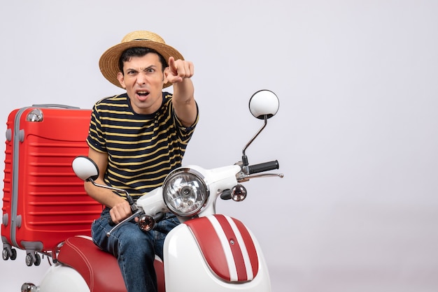 Front view young man with straw hat on moped pointing at camera