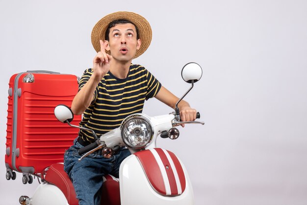 Front view of young man with straw hat on moped pointing at ceiling