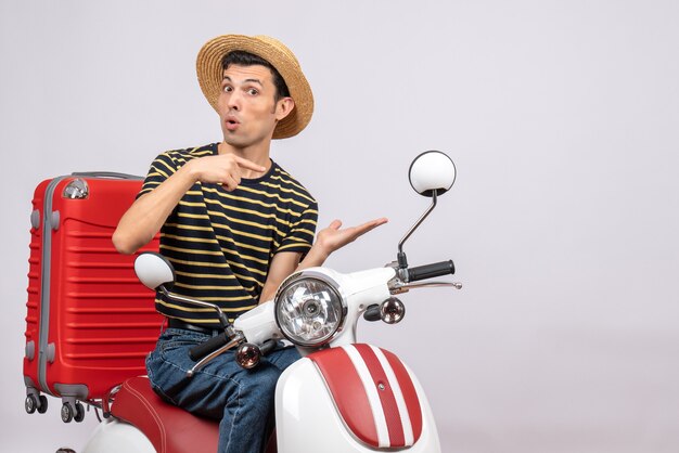 Front view of young man with straw hat on moped pointing at his hand