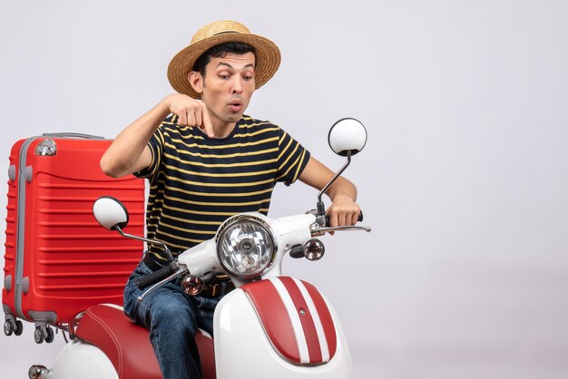 Front view of young man with straw hat on moped pointing with fingers below