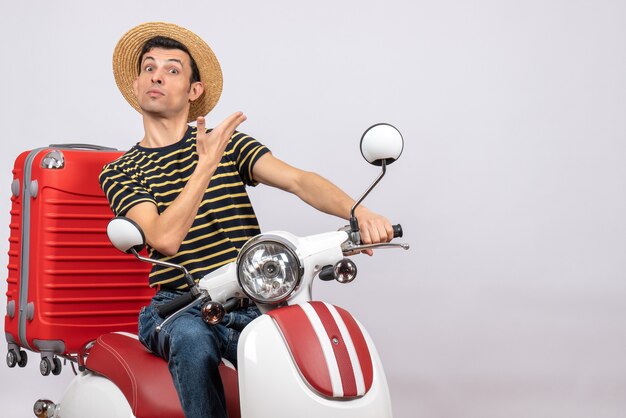 Front view of young man with straw hat on moped standing on white background