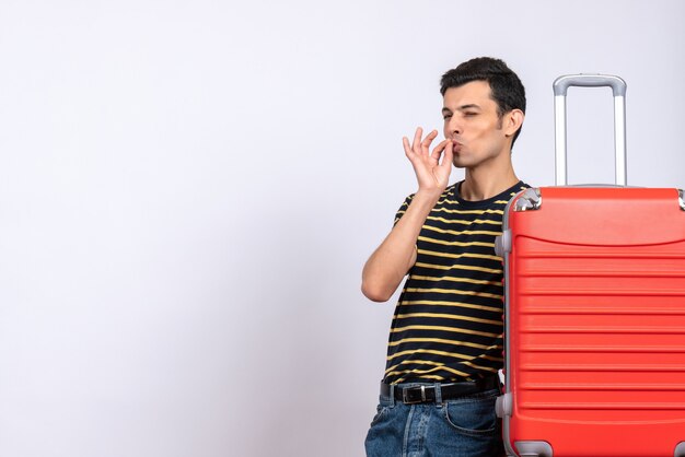 Front view young man with striped t-shirt and red suitcase making tasty sign