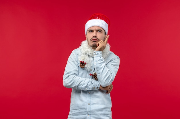 Front view of young man with thinking expression on red wall