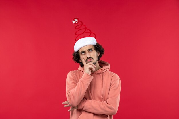 Front view of young man with thinking face on red wall