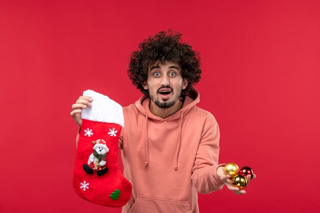 Front view of young man with toys and sock on red wall