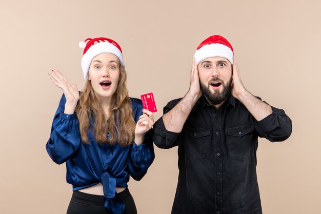 Front view of young man with woman who's holding bank card on pink wall