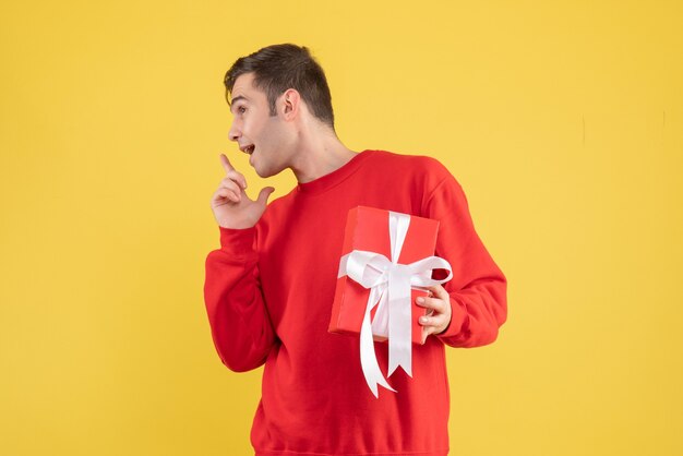 Front view young man with xmas gift standing on yellow background