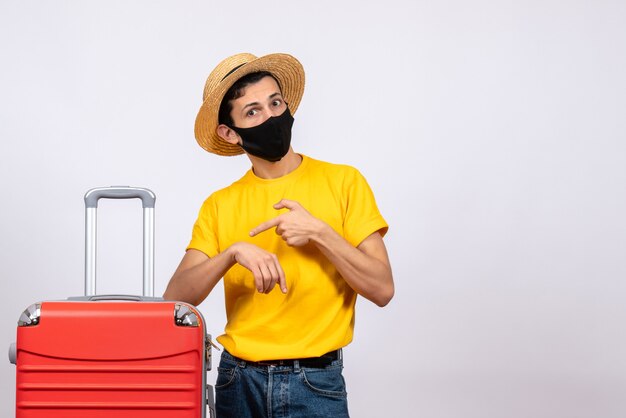 Вид спереди молодой человек с желтой футболкой и красным чемоданом спрашивает время