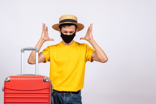 Front view young man with yellow t-shirt and red suitcase confusing