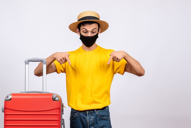 Front view young man with yellow t-shirt and red suitcase pointing at below