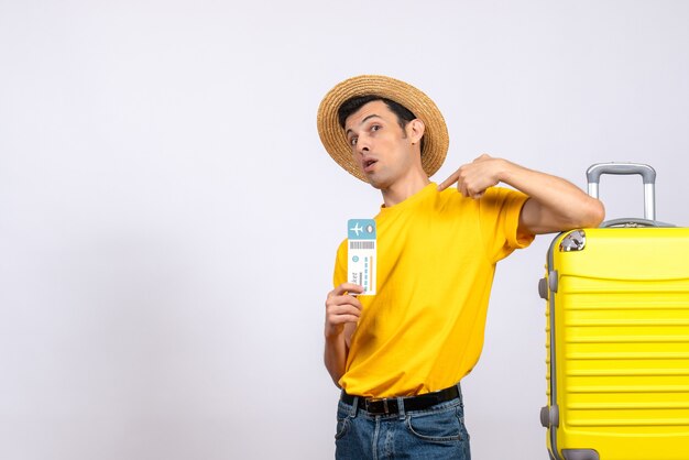 Front view young man in yellow t-shirt standing near yellow suitcase pointing at himself