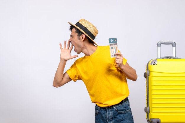 Front view young man in yellow t-shirt standing near yellow suitcase shouting