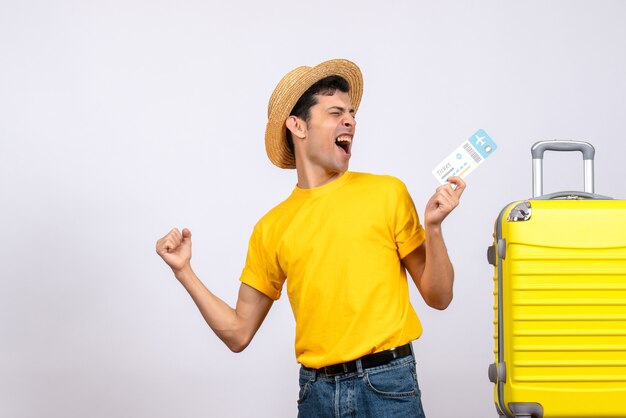 Front view young man in yellow t-shirt standing near yellow suitcase showing his happiness