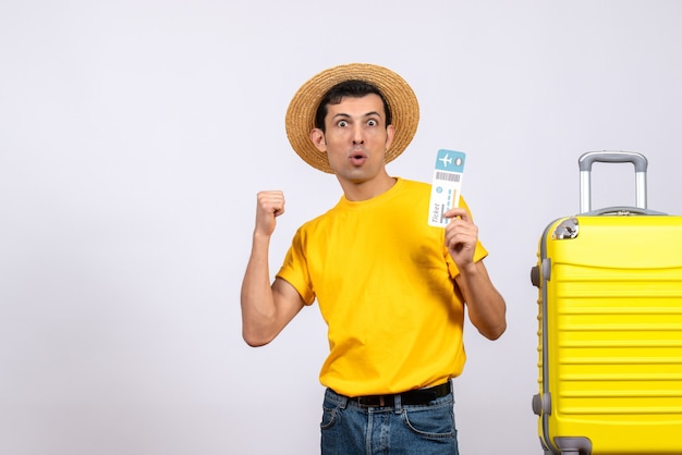 Front view young man in yellow t-shirt and straw hat standing near yellow suitcase