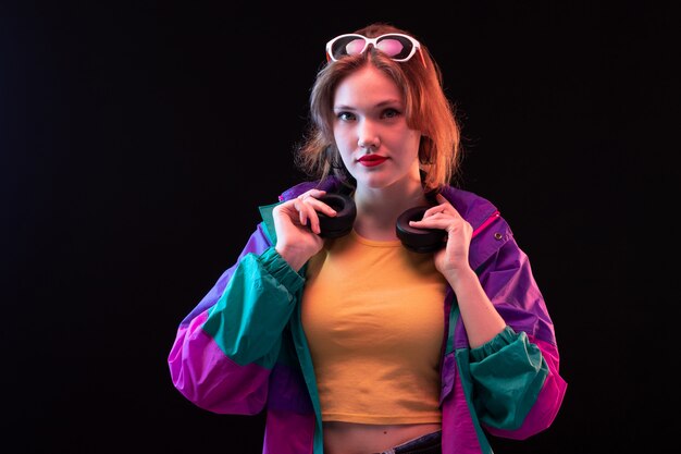 A front view young modern lady in colorful coat orange t-shirt with black earphones and sunglasses posing