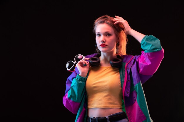 A front view young modern lady in colorful coat orange t-shirt with black earphones and sunglasses posing