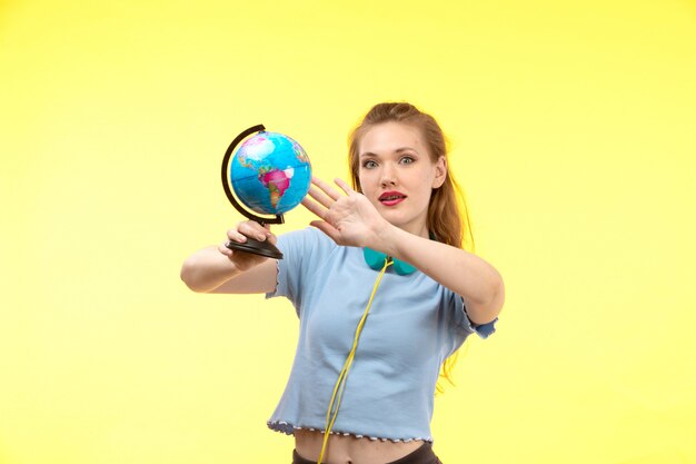A front view young modern woman in blue shirt black trousers in colorful earphones holding little globe