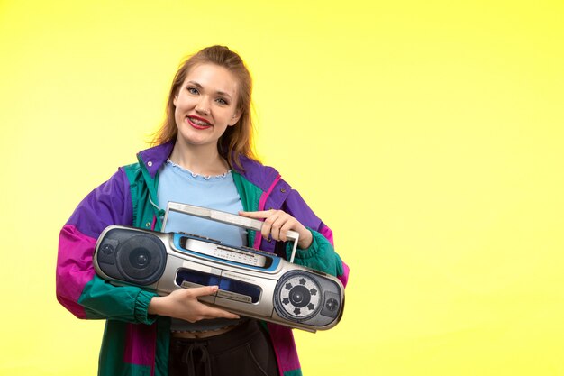 A front view young modern woman in blue shirt black trousers colorful jacket smiling posing holding tape-recorder