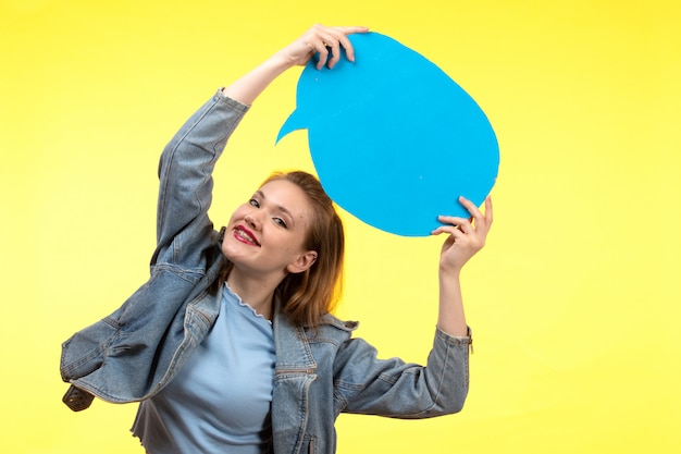 Foto gratuita una giovane donna moderna di vista frontale in pantaloni blu camicia nera e cappotto jean in posa espressione felice sorridente con cartello di carta blu