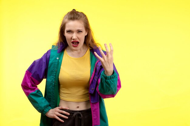 A front view young modern woman in yellow shirt black trousers and colorful jacket posing displeased