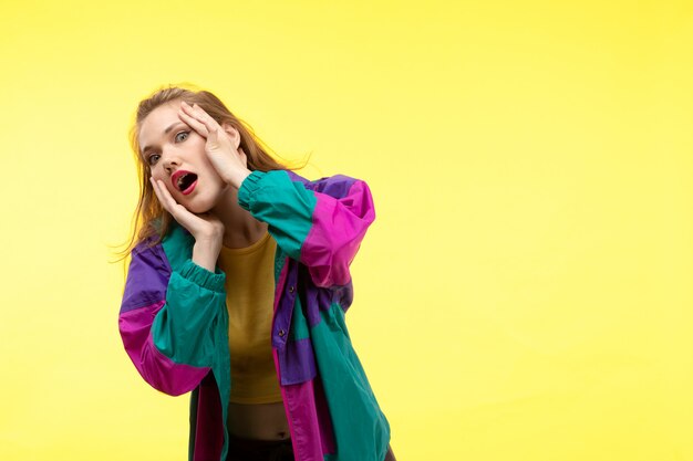 A front view young modern woman in yellow shirt black trousers and colorful jacket posing surprised frightening expression