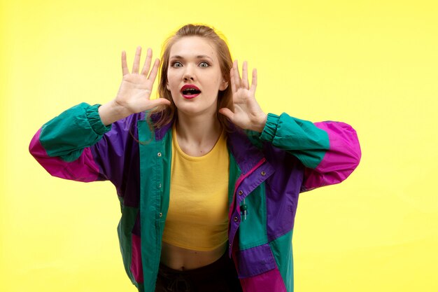 A front view young modern woman in yellow shirt black trousers and colorful jacket posing surprised
