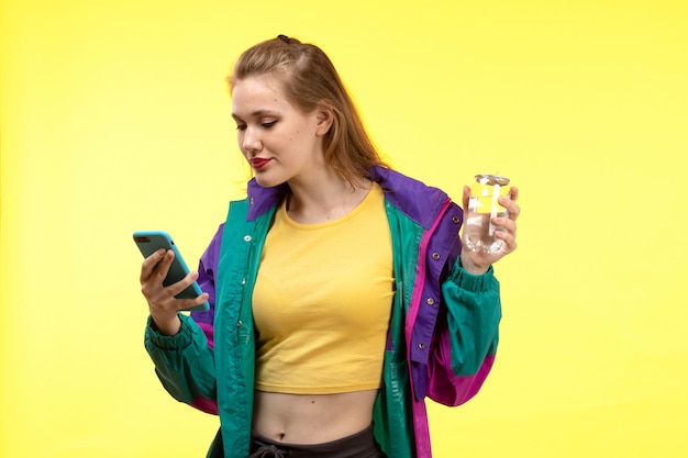 A front view young modern woman in yellow shirt black trousers and colorful jacket using her phone