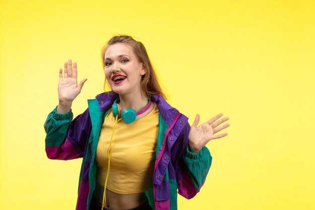 A front view young modern woman in yellow shirt black trousers and colorful jacket with colored earphones posing happy expression