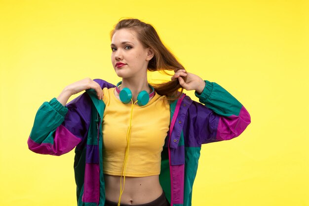 A front view young modern woman in yellow shirt black trousers and colorful jacket with colored earphones posing