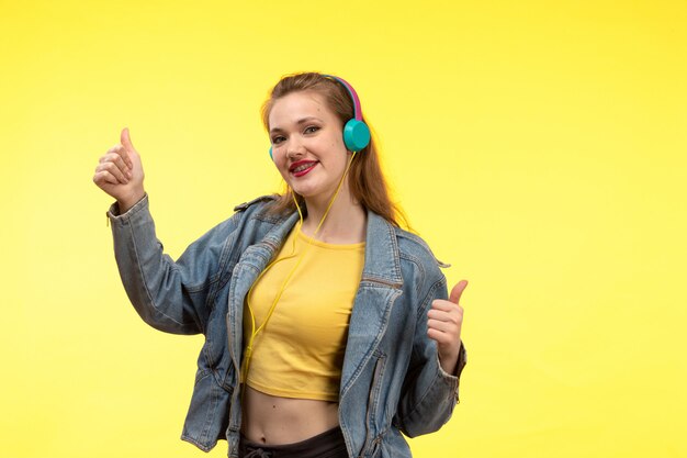 음악을 듣고 컬러 이어폰과 노란색 셔츠 검은 바지와 진 코트의 전면보기 젊은 현대 여성