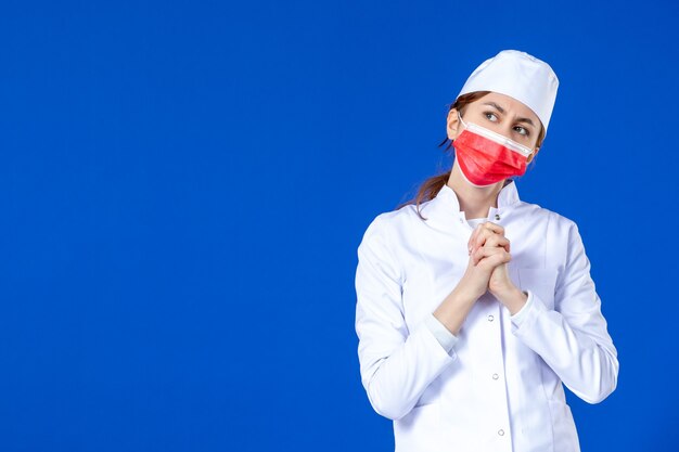 파란색 벽에 빨간 마스크와 의료 소송에서 전면보기 젊은 간호사