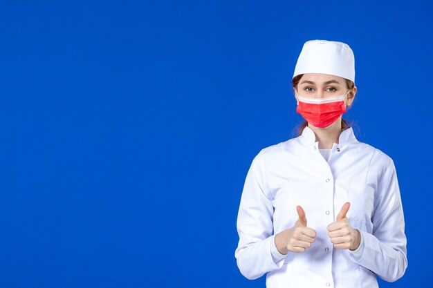 Front view of young nurse in medical suit with red mask on blue 