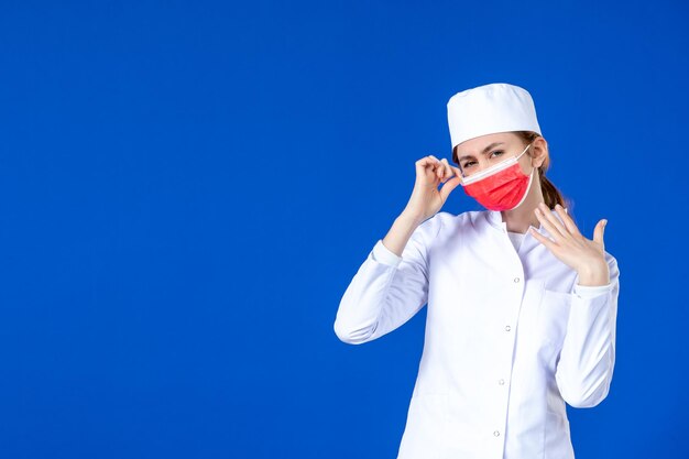 Front view of young nurse in medical suit with red mask on blue 