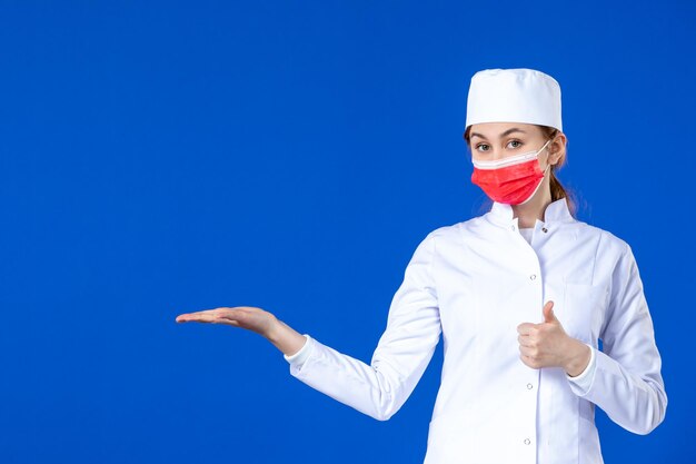Front view of young nurse in medical suit with red mask on blue 