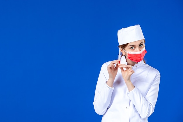 赤いマスクと青い壁に彼女の手で注射と医療スーツを着た若い看護師の正面図