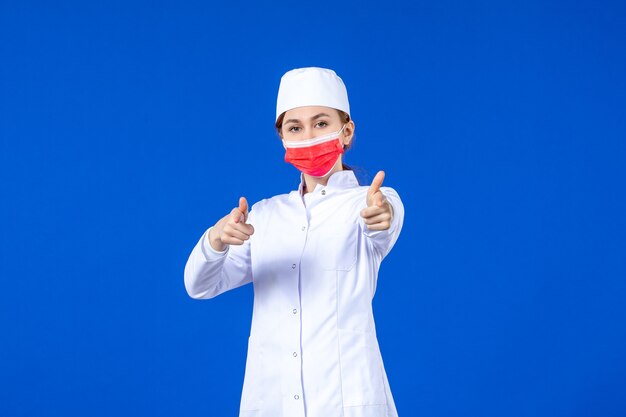 Front view young nurse in medical suit with red protective mask on blue wall