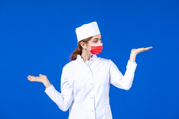 Front view young nurse in medical suit with red protective mask on blue wall