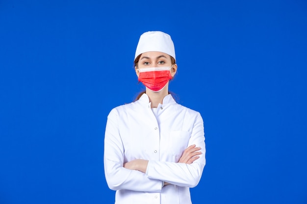 Front view young nurse in medical suit with red protective mask on blue wall