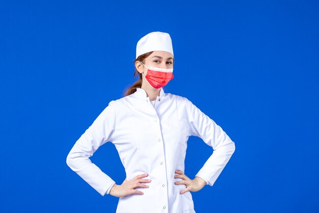 Front view young nurse in medical suit with red protective mask on blue wall