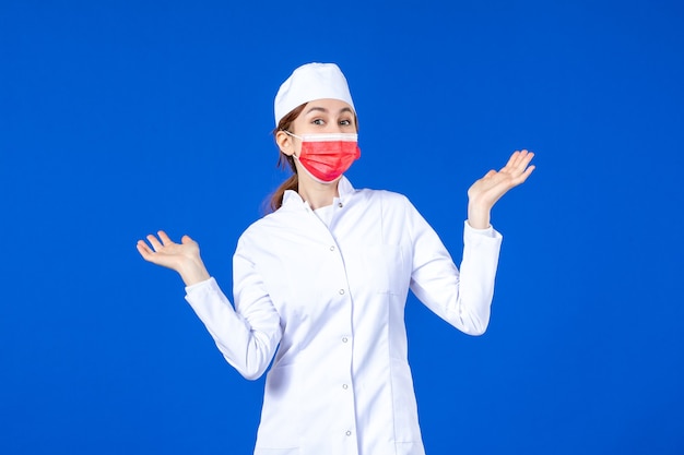 Front view young nurse in medical suit with red protective mask on blue wall