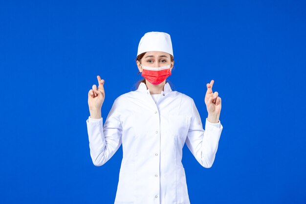 Front view young nurse in medical suit with red protective mask on blue wall