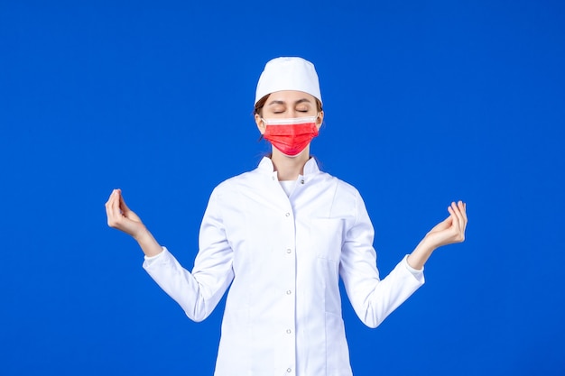 파란색 벽에 빨간색 보호 마스크와 의료 소송에서 전면보기 젊은 간호사