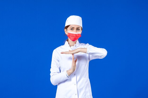 Front view young nurse in medical suit with red protective mask on blue wall