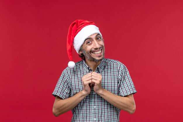 Вид спереди молодой человек с улыбающимся выражением лица на красной стене праздники новогодний красный