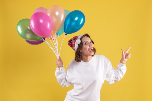 Front view young pretty female holding balloons on a yellow christmas woman new year color emotion