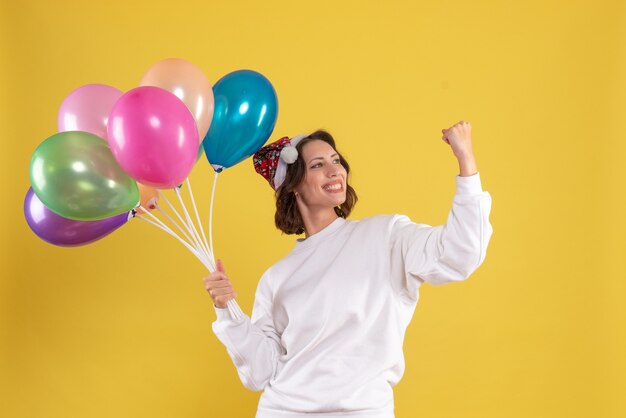 Вид спереди молодая красивая женщина держит воздушные шары на желтом цвете рождество новый год эмоция женщина